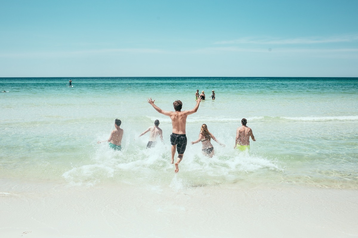 Várias pessoas mergulhando e brincando nas ondas do mar, em beira da praia.