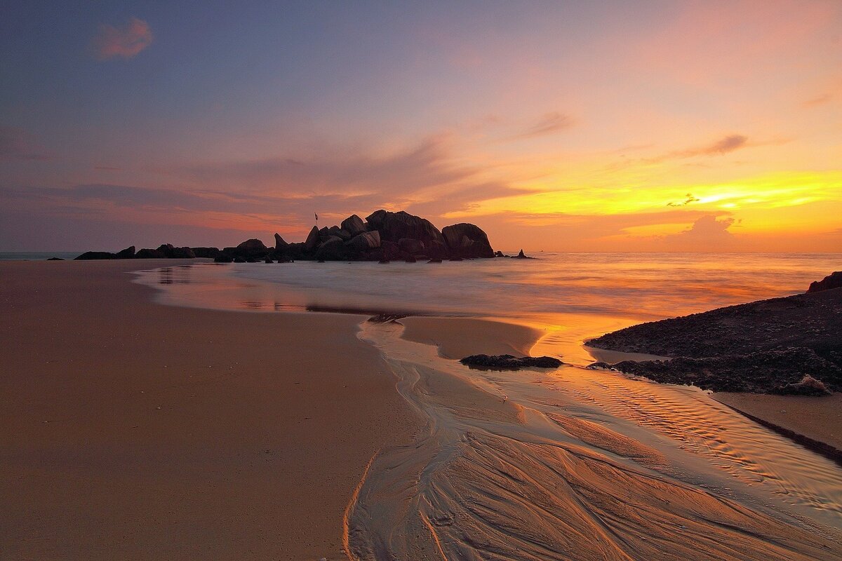 Pôr do sol alaranjado e arroxeado ocorrendo em horizonte de praia deserta.
