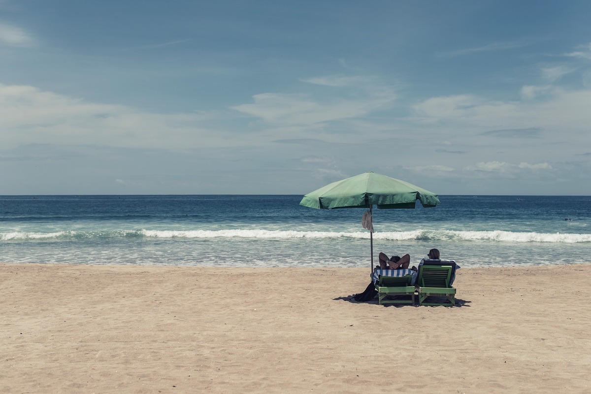 Duas pessoas deitadas em cadeira de praia em frente ao mar, em uma praia deserta.