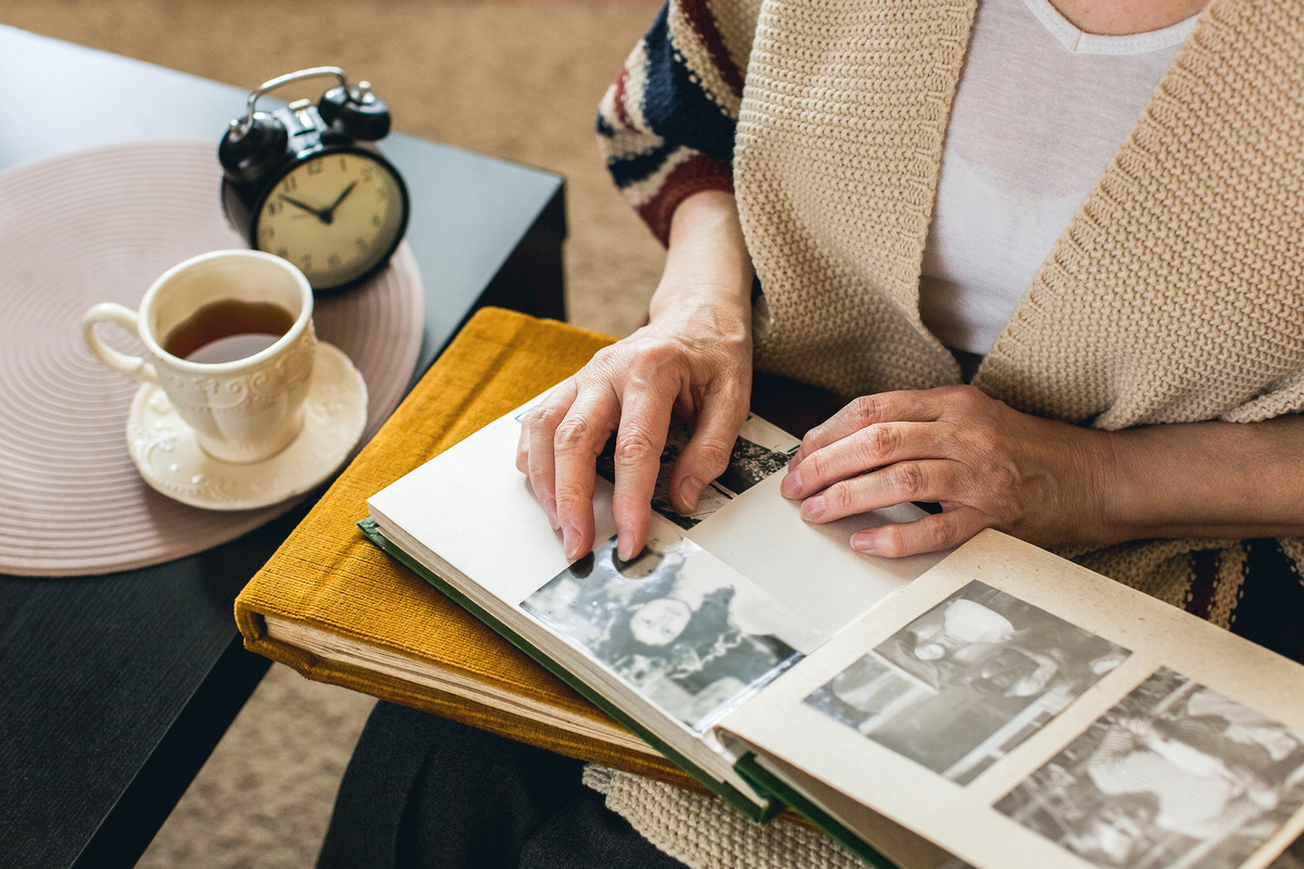 Mulher olhando para álbum de fotos enquanto tem uma xícara de chá ao seu lado, simbolizando sonhar com foto de falecido.