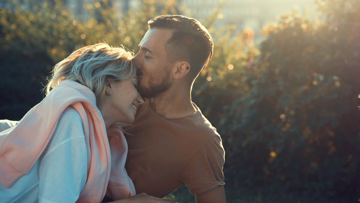 Homem beijando testa de mulher enquanto ela sorri, representando o carinho encontrado nos homens de Libra.