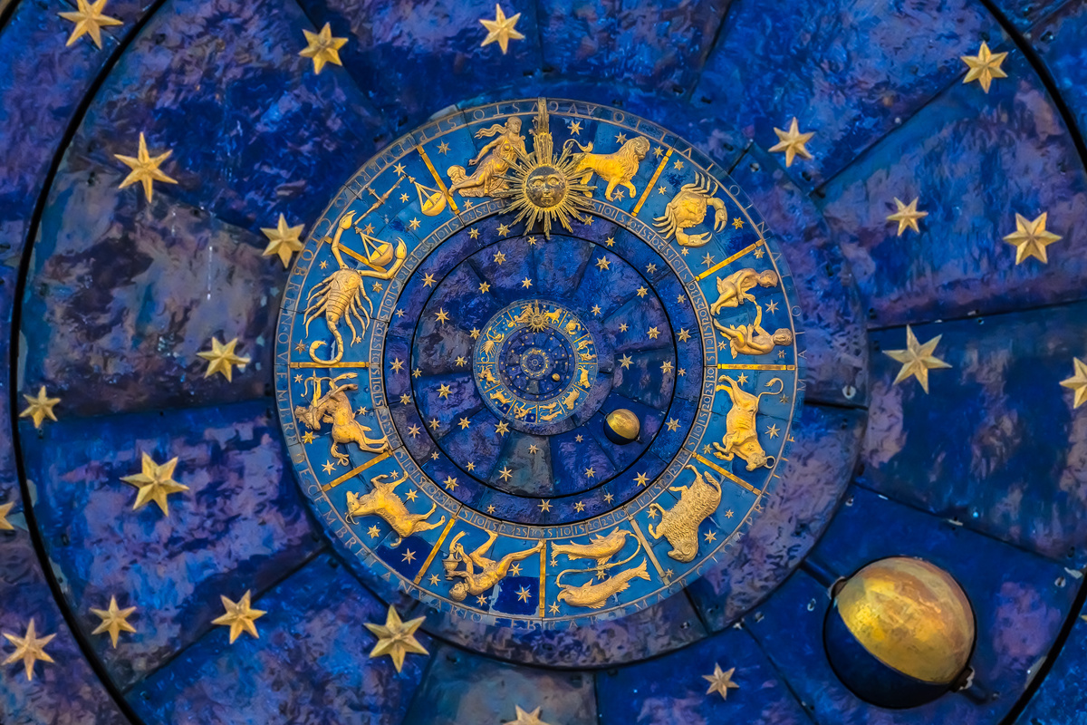 Mandala astrológica esculpida em parede, em cores azul e com detalhes de signos e astros em dourado. 