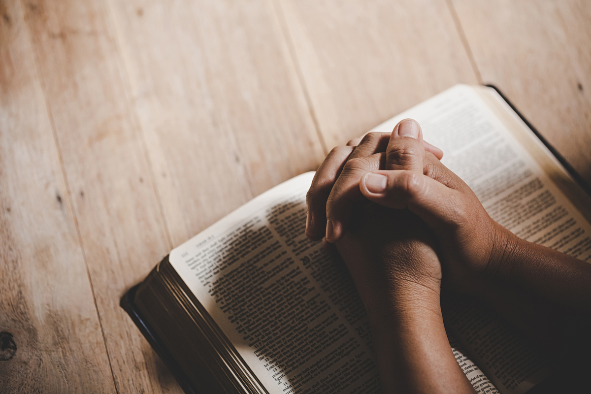 Mãos de pessoa rezando em cima de Bíblia