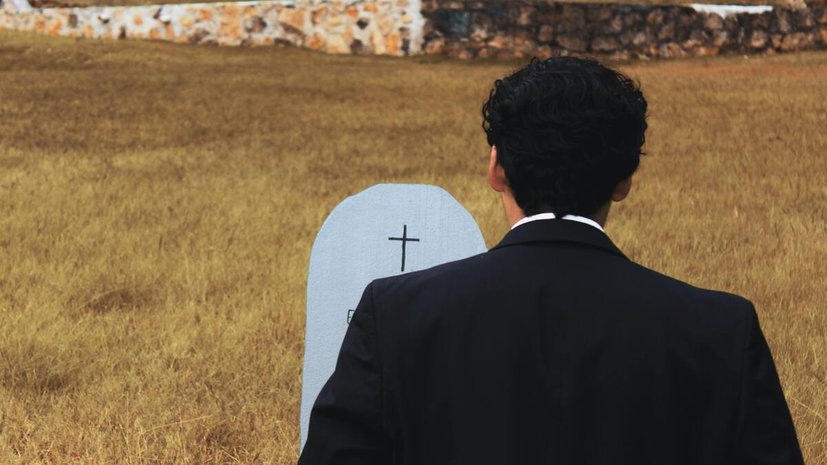 Homem de terno em frente a lápide em cemitério.