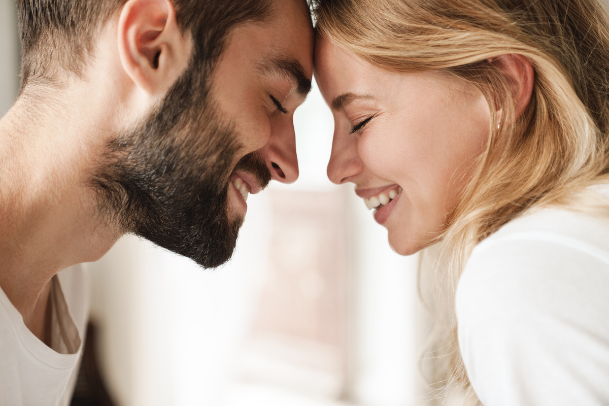 Homem e mulher sorrindo enquanto apoiam as testas uma na outra, representando a intimidade de Áries e Aquário.
