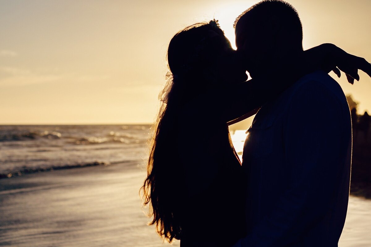 Sombra de homem e mulher se beijando ao por do sol em frente ao mar, representando o casal de Gêmeos e Peixes.