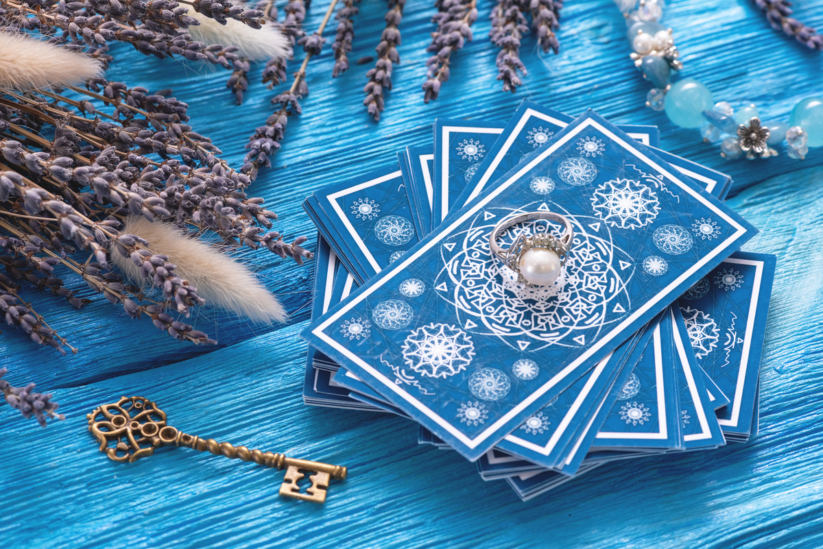 Cartas de tarot azuis em superfície de toalha azul, com ervas em volta, além de um anel e uma chave.