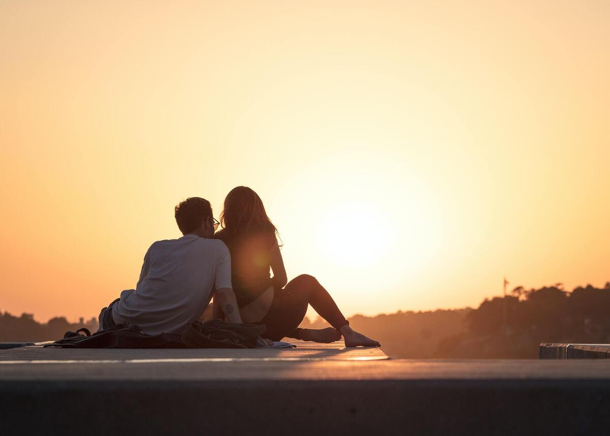 Homem e mulher sentados observando o pôr do sol.