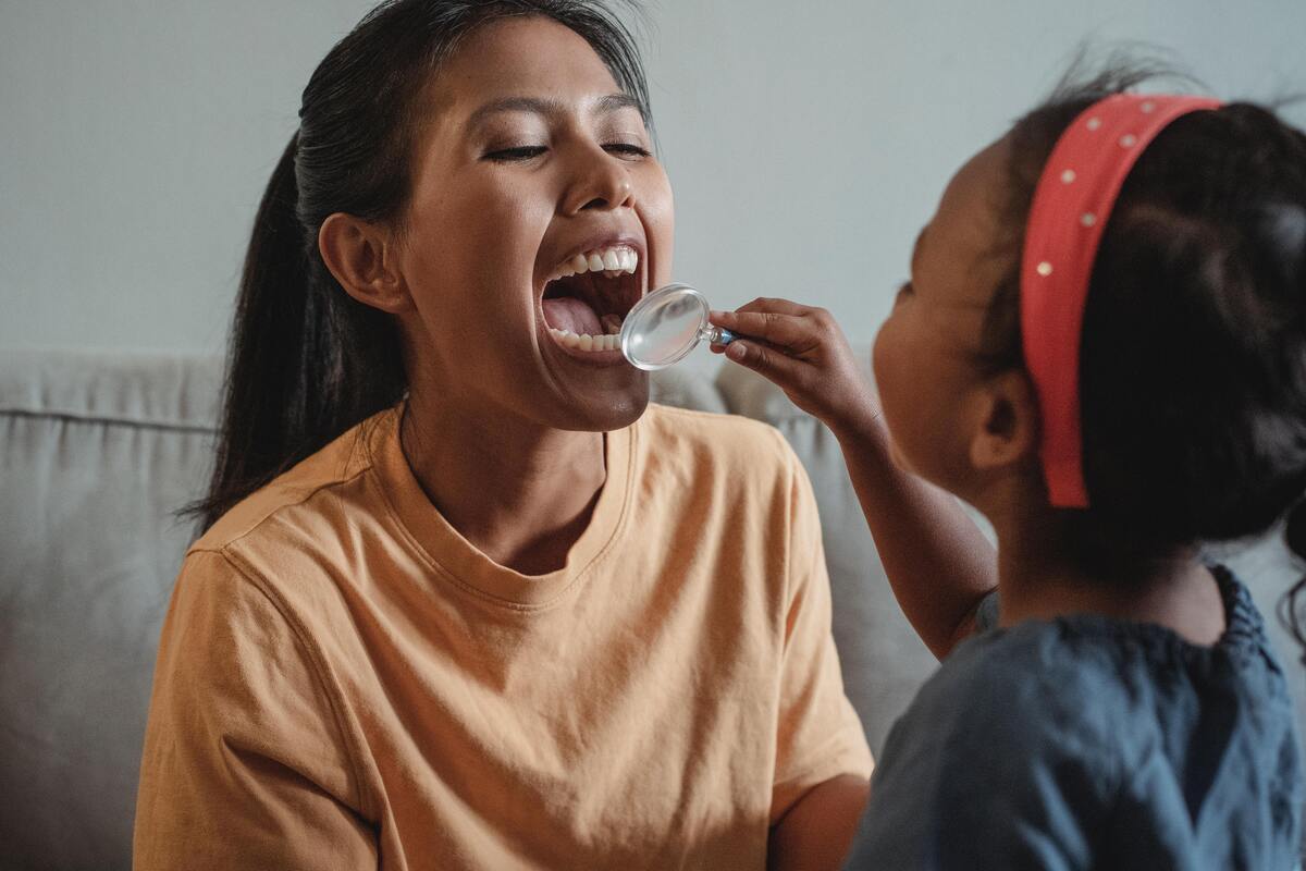 Menina observa os dentes da mãe com uma lupa.