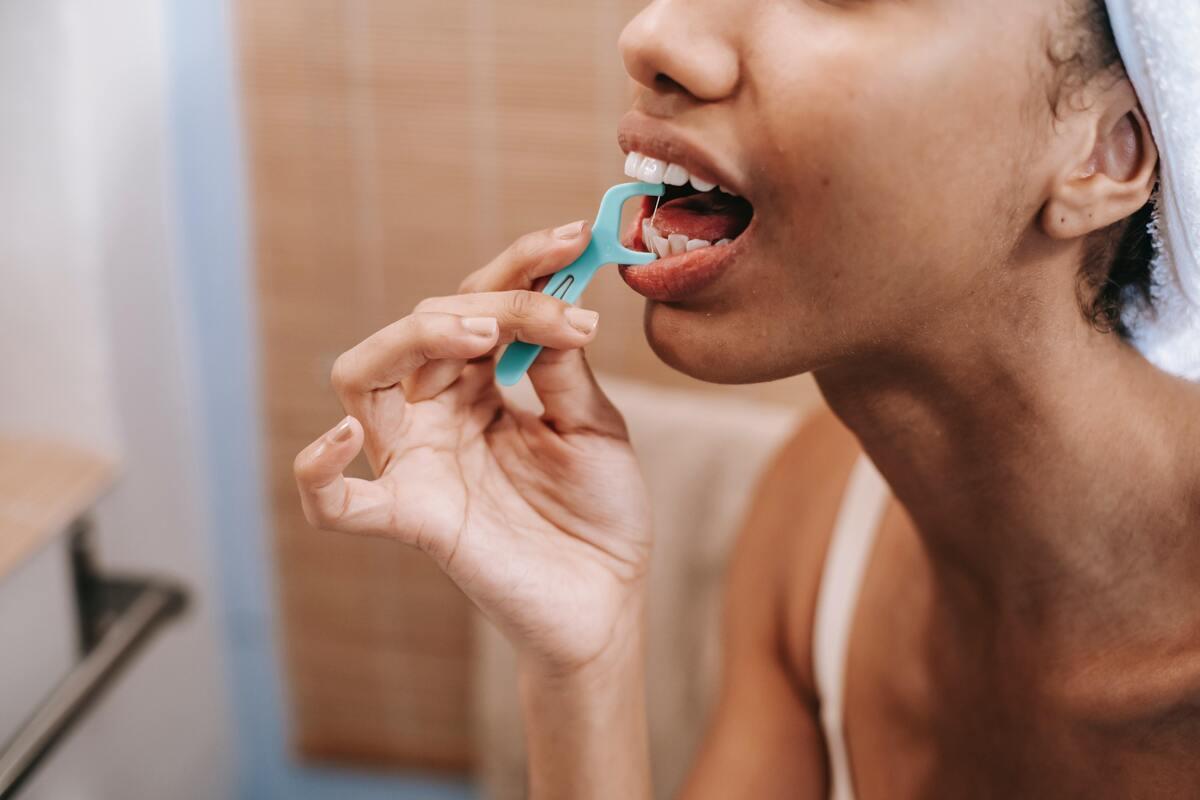 Mulher usando fio dental em seus dentes.