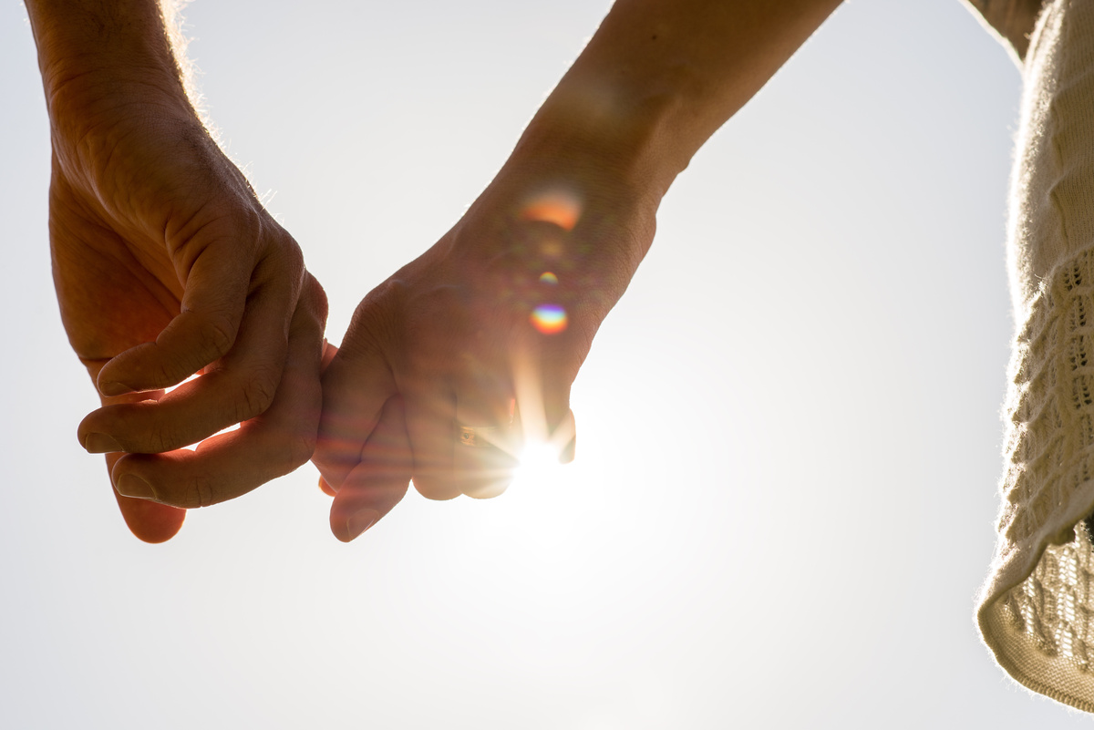 Duas mãos dadas em frente à luz do sol, representando a ligação entre Virgem e Escorpião entre si ou com outras pessoas.
