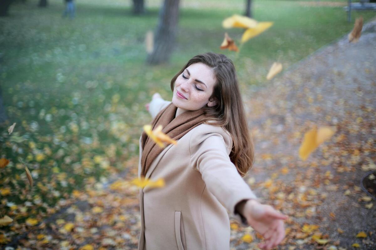 Mulher sorrindo no parque cercada por folhas secas.