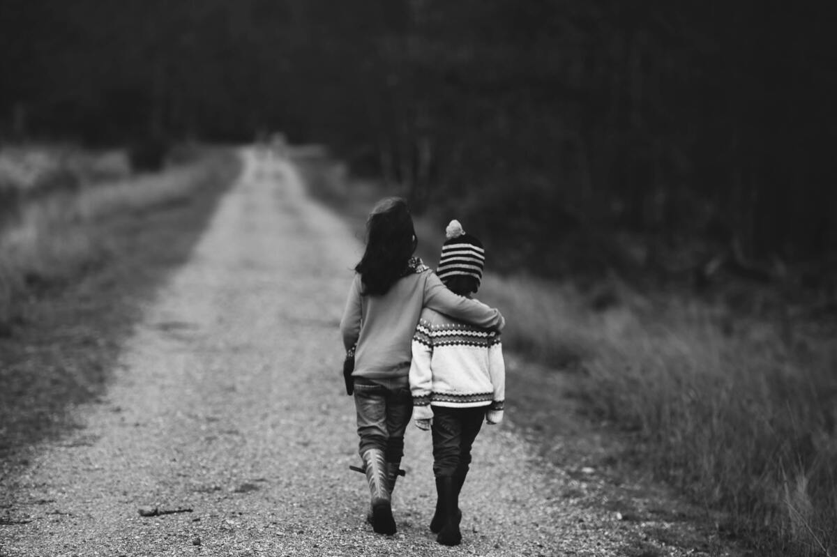 Duas crianças abraçadas caminhando em estrada.