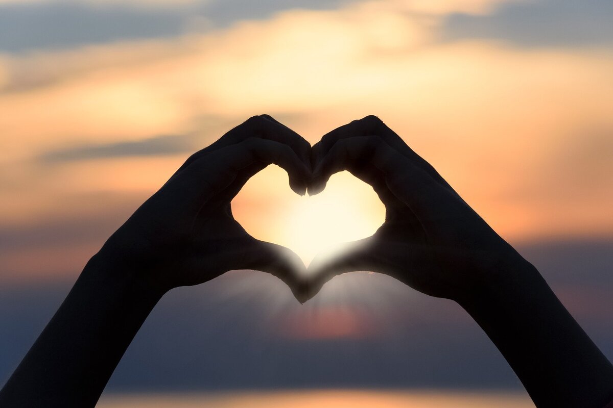 Duas mãos unidas em formato de coração, em frente ao por do sol, representando o amor resultante da conquista de um taurino.