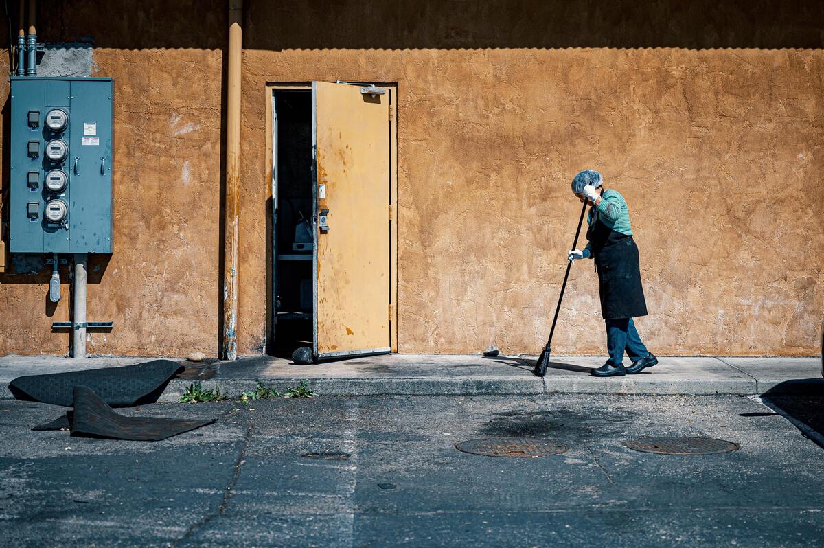 Mulher limpando calçada com uma vassoura.