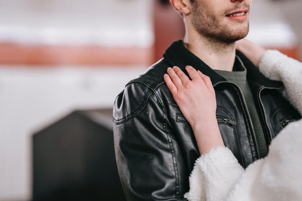 Homem usando jaqueta de couro enquanto uma mulher está com aos mãos em seus ombros.