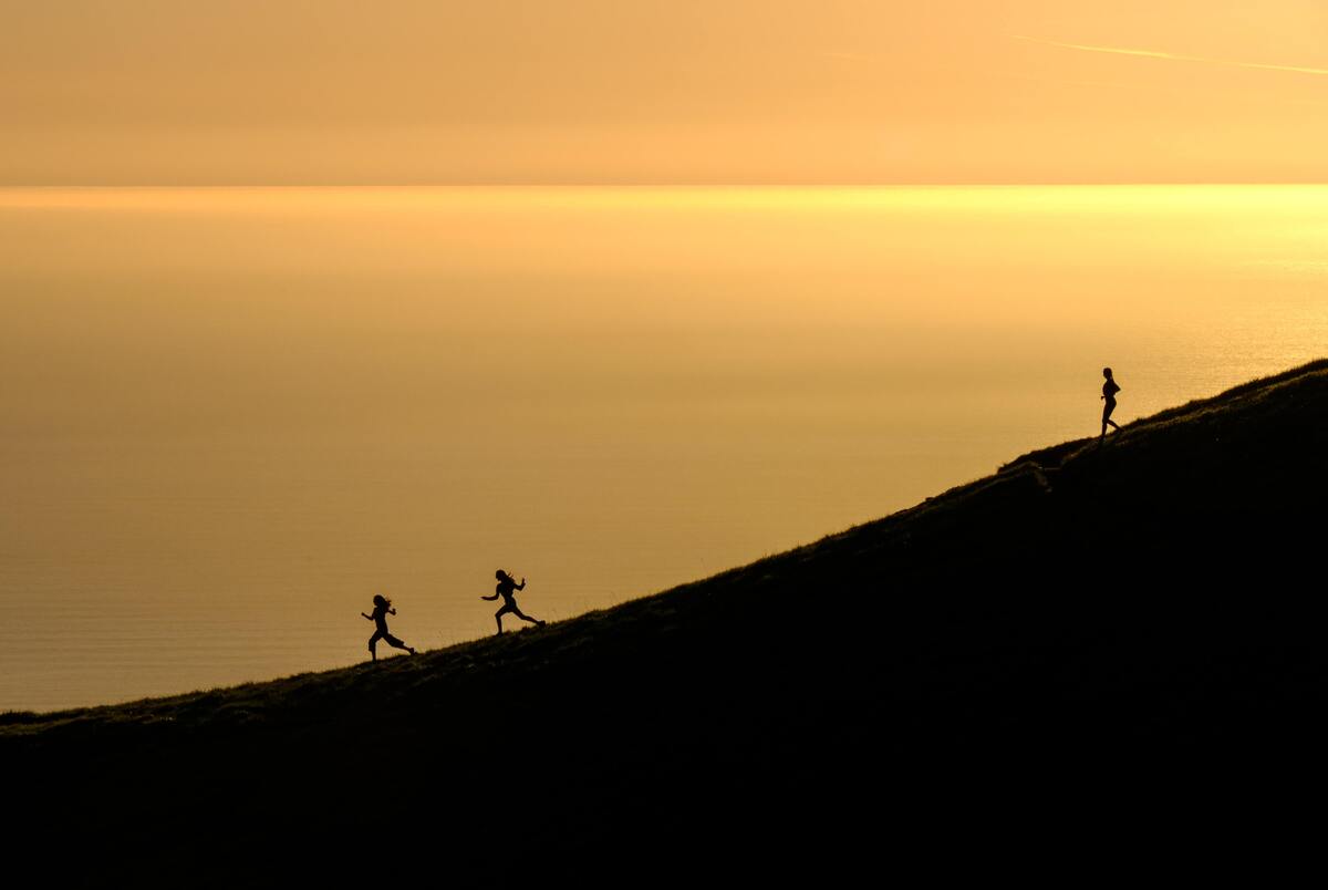 Três silhuetas caminhando sobre uma montanha. 