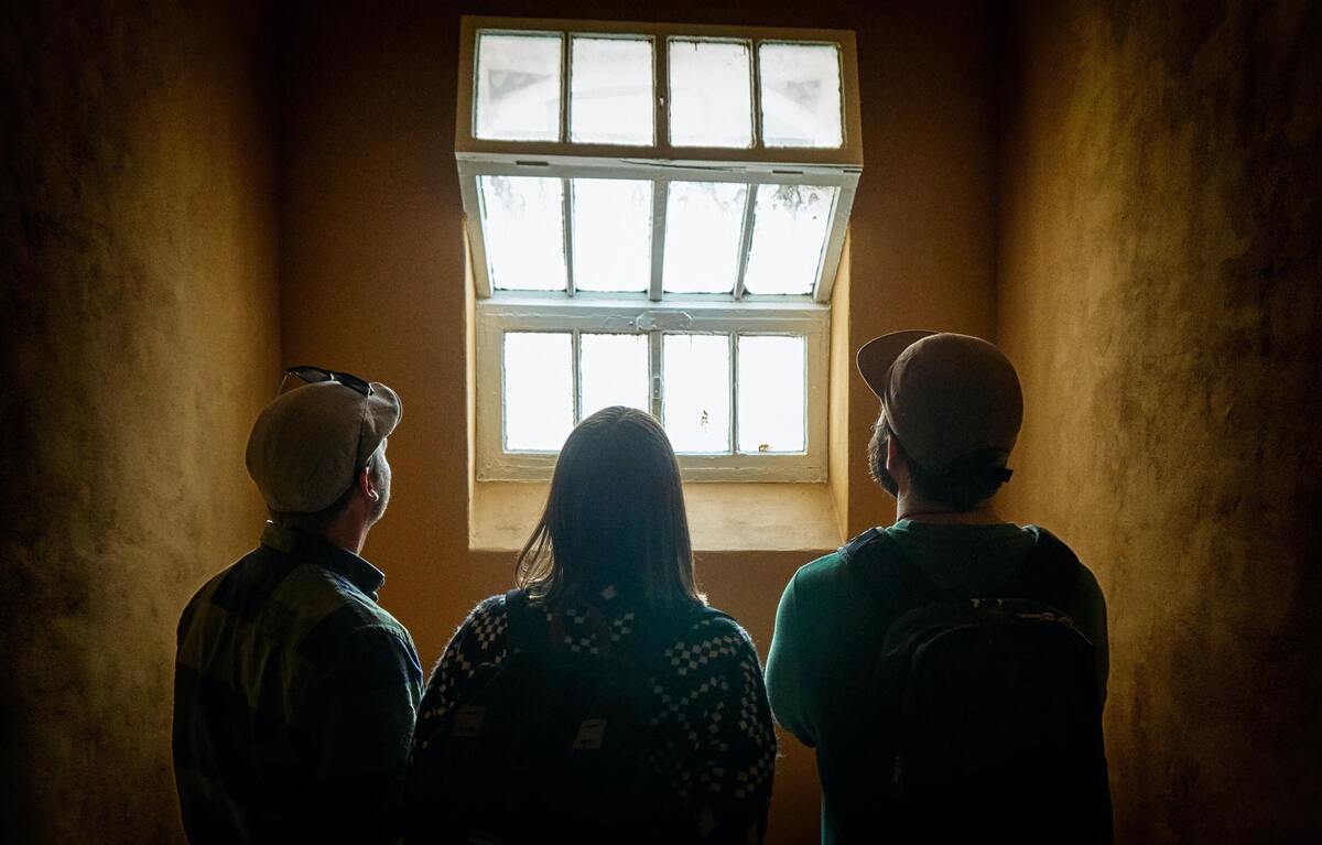 Três pessoas de costas olhando para uma janela.