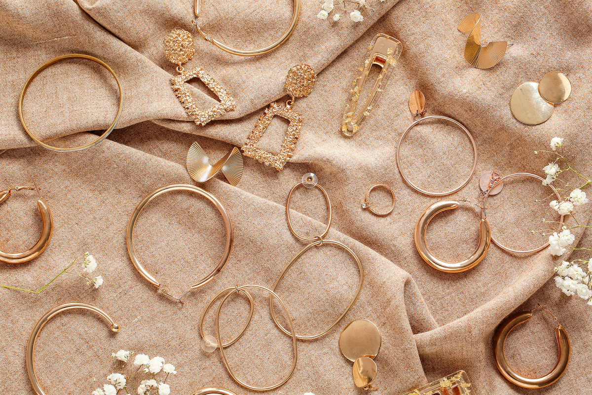 Diversos brincos de ouro estendidos em superfície de tecido dourado.