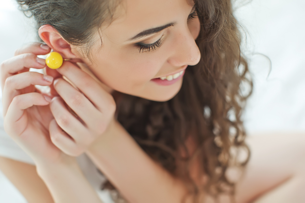 Mulher colocando brinco amarelo na orelha enquanto sorri.