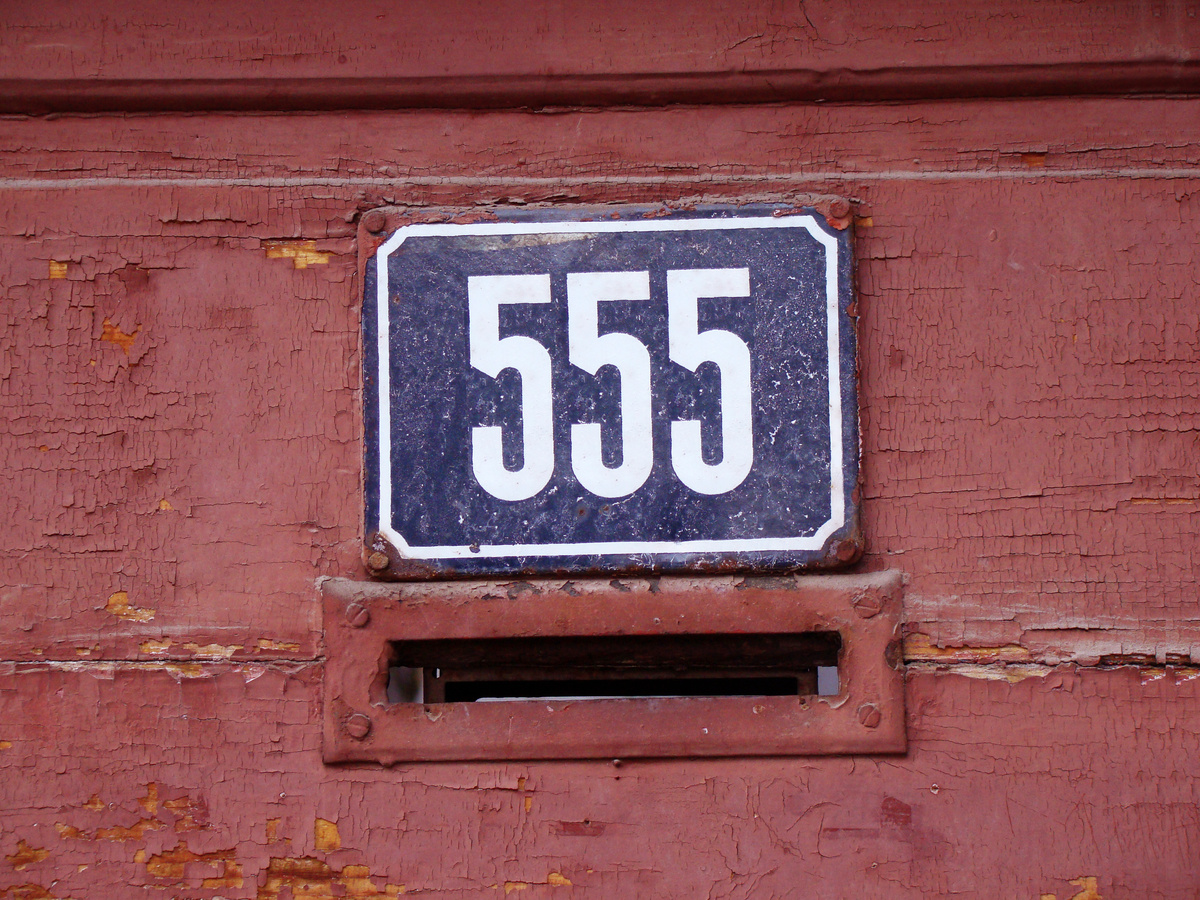 Placa azul com número 555, encostada em parede vermelha.