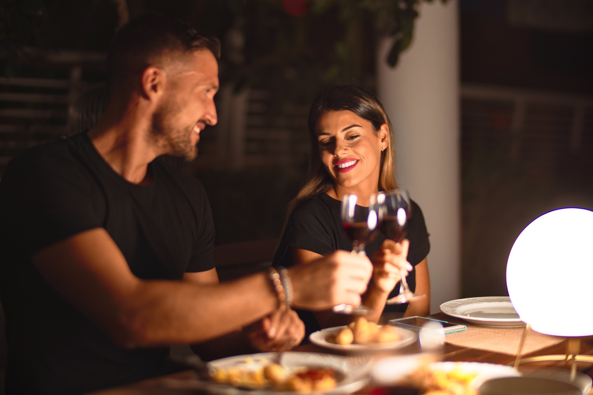 Homem e mulher em jantar a luz de velas enquanto brindam com taça de vinho, representando uma forma de conquistar um taurino: através de uma boa comida.