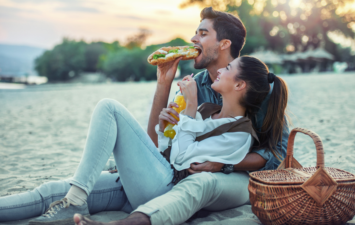 Homem e mulher em piquenique diante da praia, comendo juntos, representando um taurino conquistado por um novo amor.