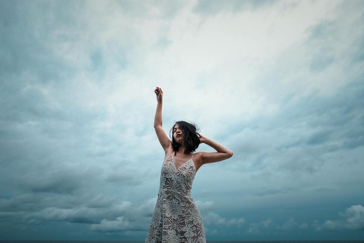 Mulher dançando sozinha com o céu ao fundo.