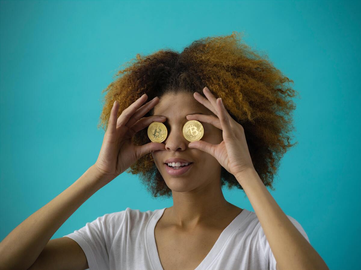 Mulher segurando duas moedas no lugar dos olhos.