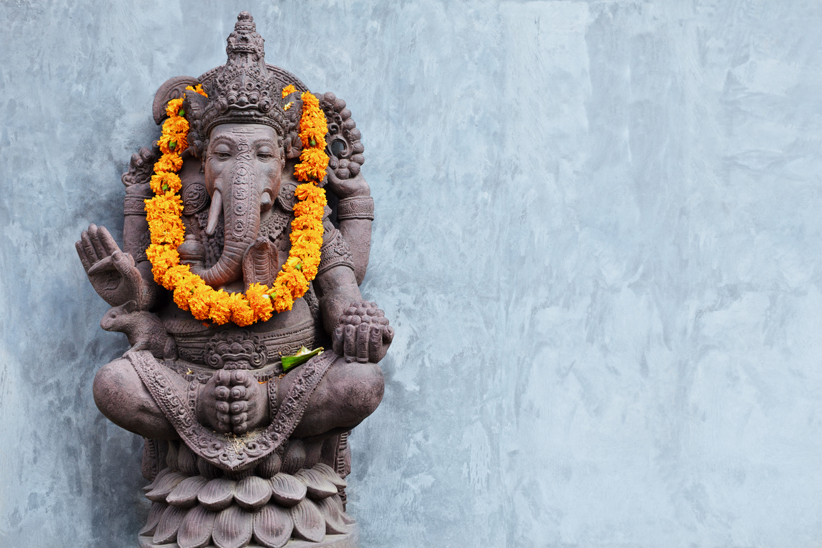 Estátua de pedra de elefante, com coroa de flores laranjas, representando Ganesha.