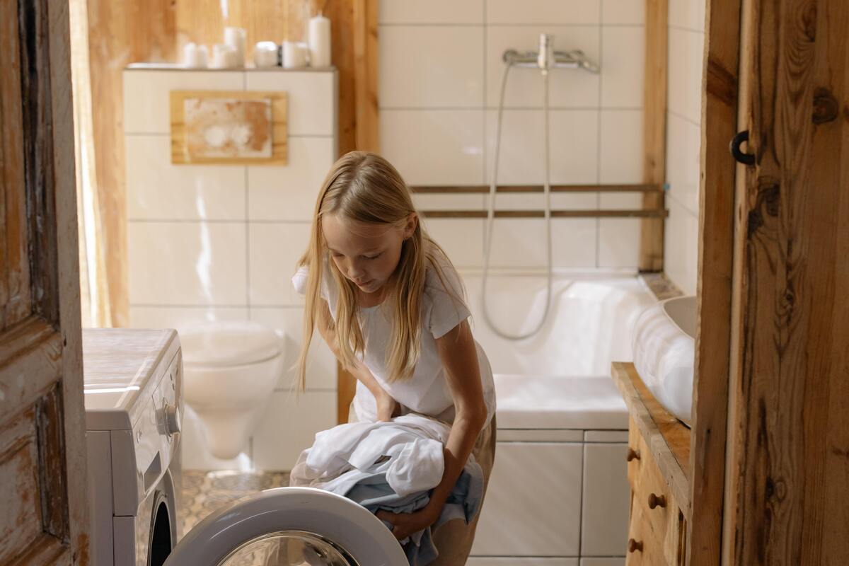 Menina colocando roupas na máquina de lavar.