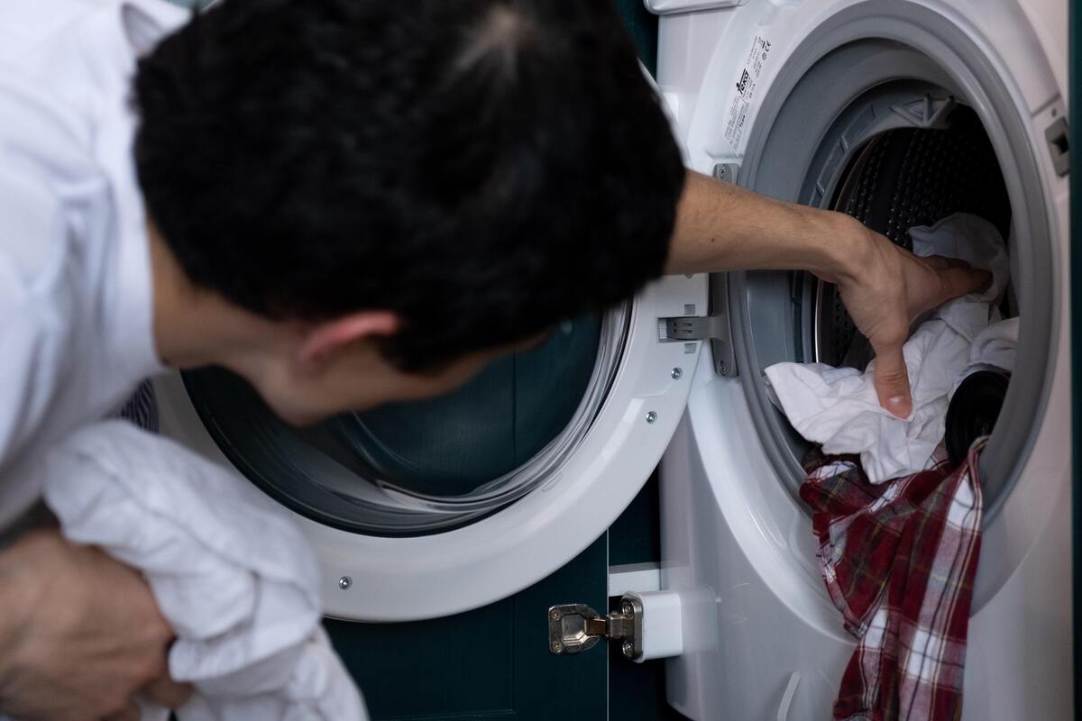 Homem tirando roupas da máquina de lavar.