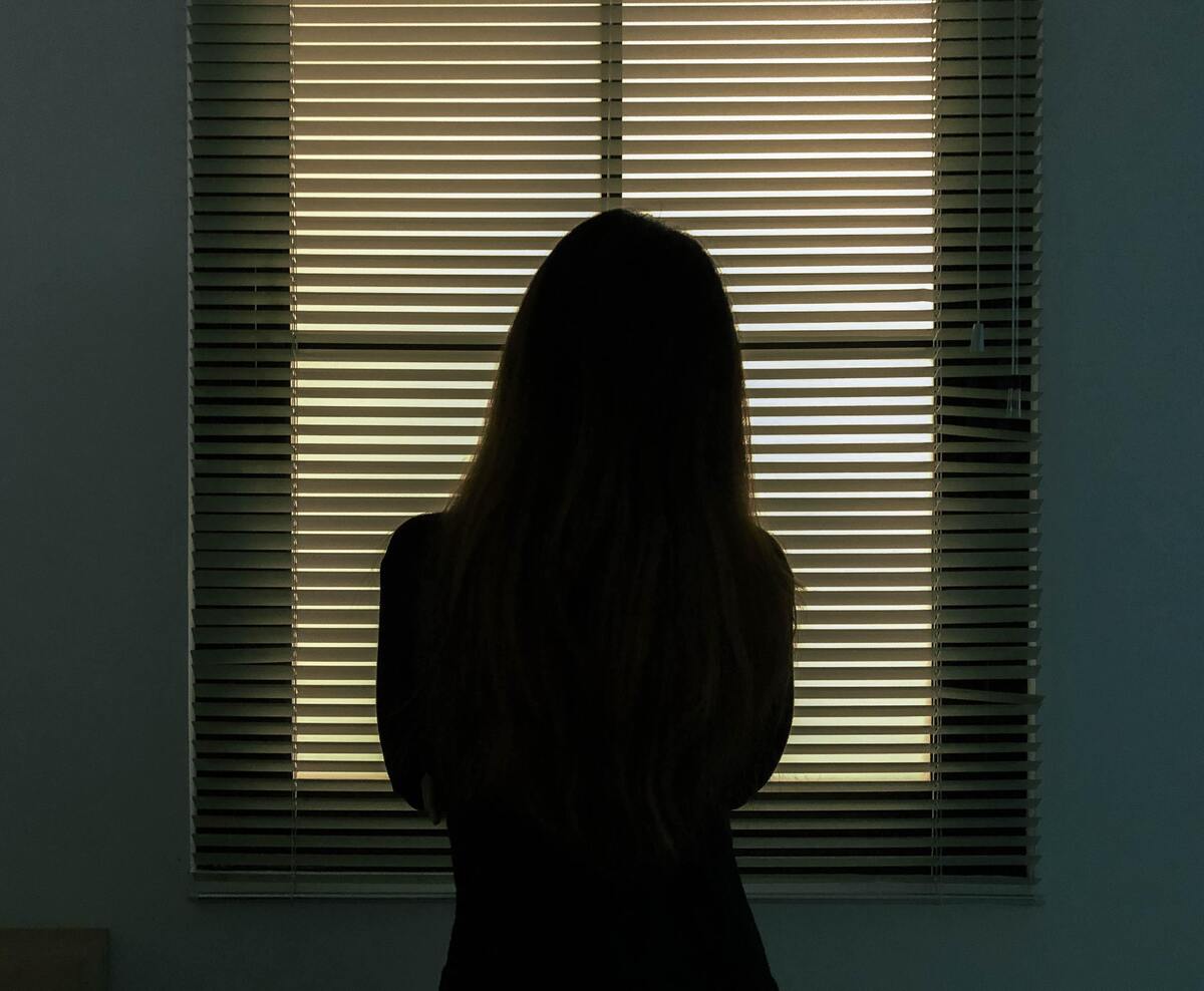 Silhueta de uma mulher em frente à janela fechada.