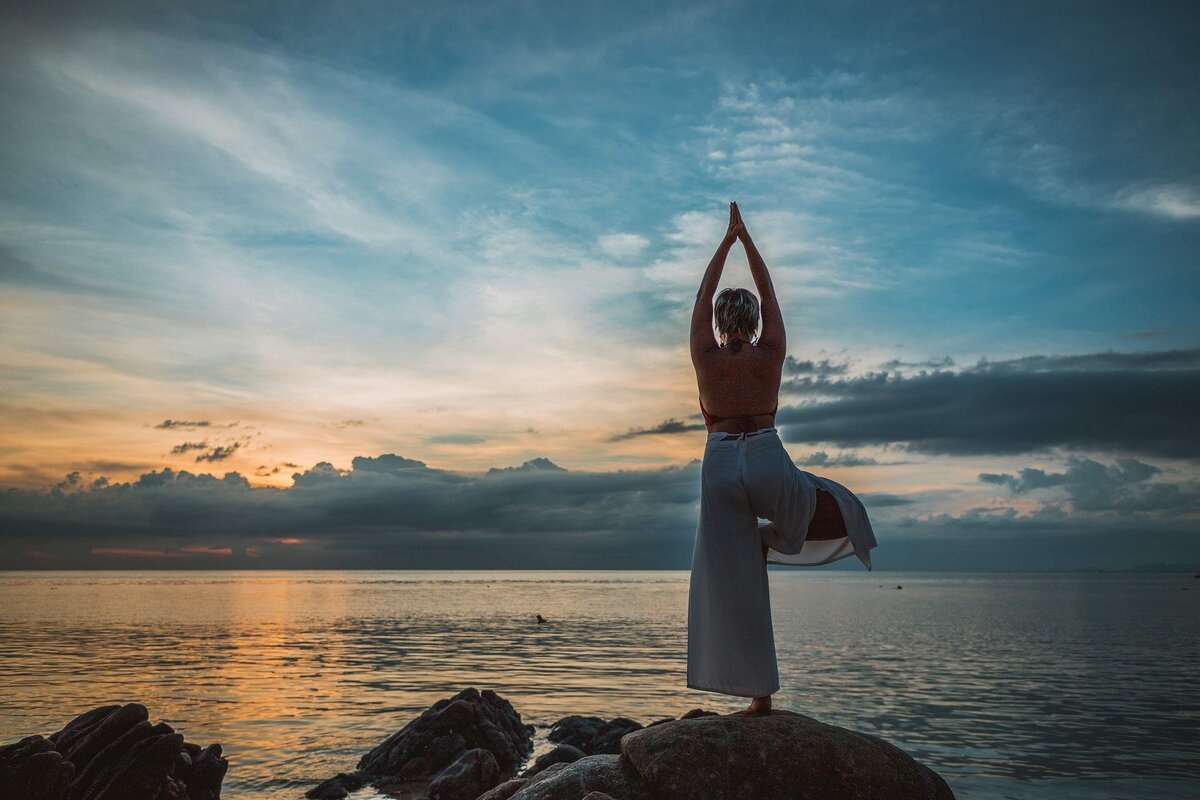 Mulher fazendo pose de yoga em meio à paisagem de um pôr do sol.