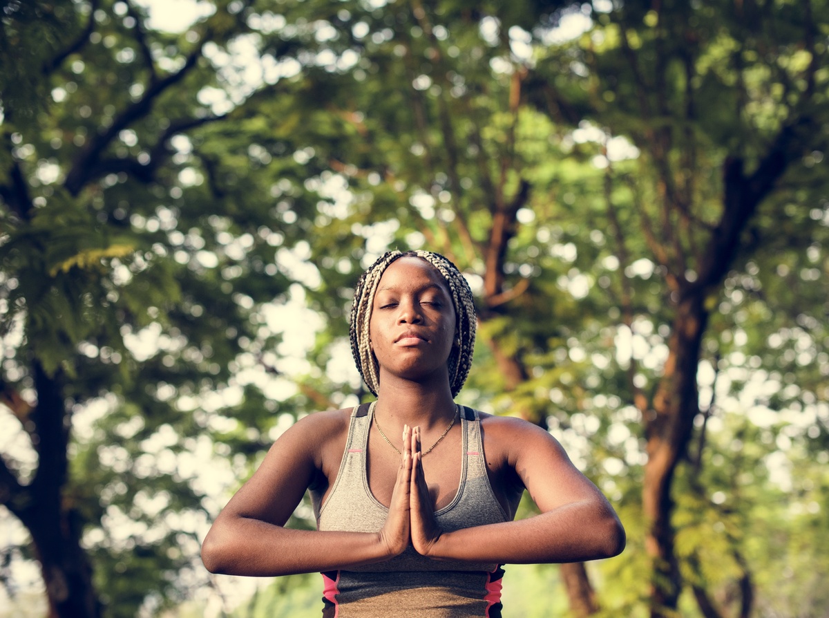 Mulher com as mãos unidas ao centro do seu tronco, em pose de meditação.
