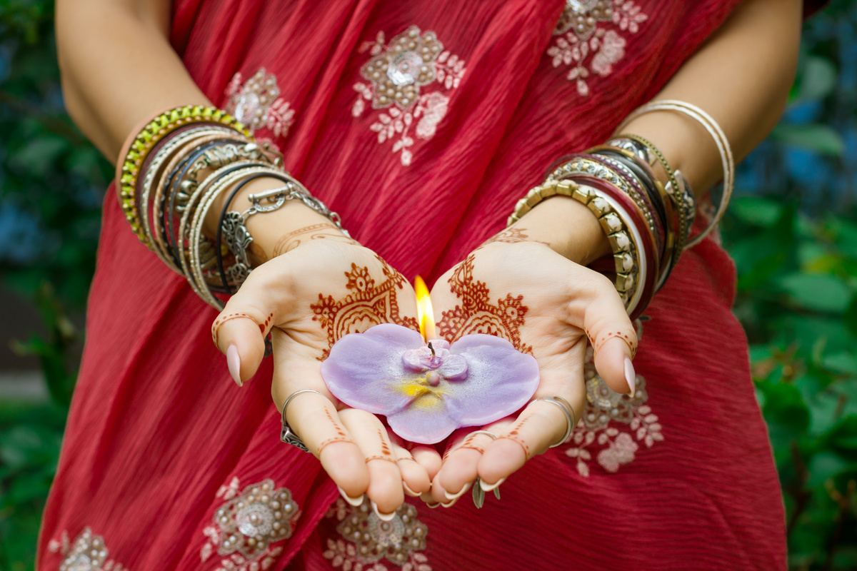 Mulher com roupas características da cultura indiana segurando uma vela com formato de flor de lótus nas duas mãos, representando a origem da Ayurveda.