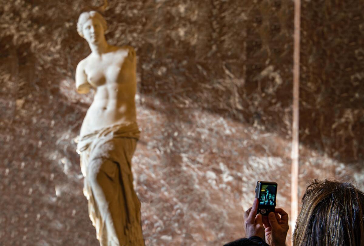 Mulher tirando foto de uma estátua de Vênus.
