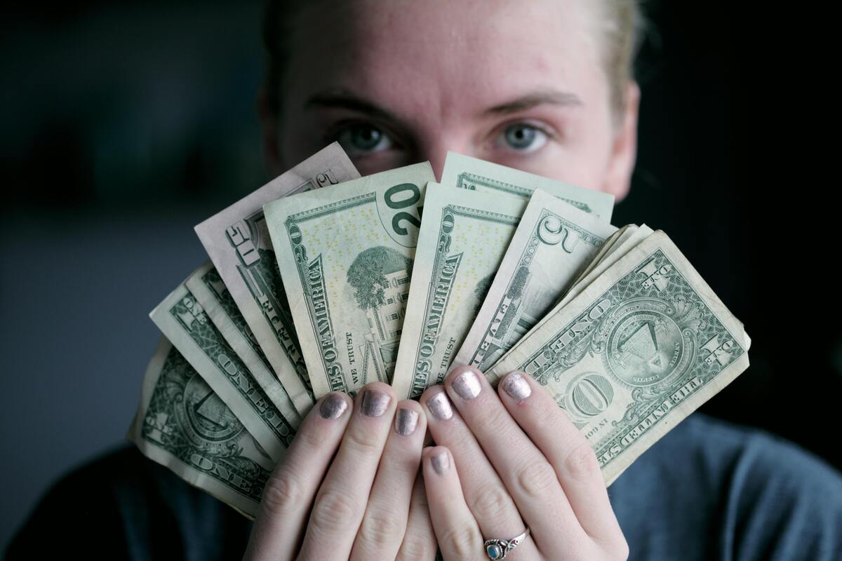 Mulher segurando várias notas de dólar na frente de seu rosto.