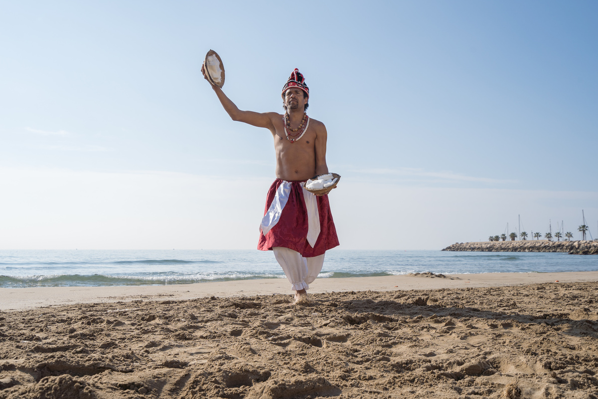 Homem vestido de Xangô dançando em praia.