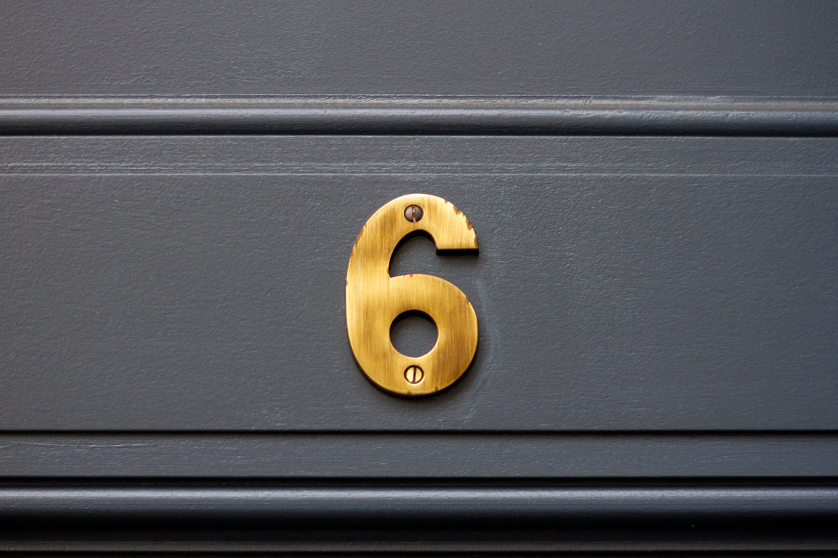 Número 6 em dourado parafusado em porta de madeira preta.