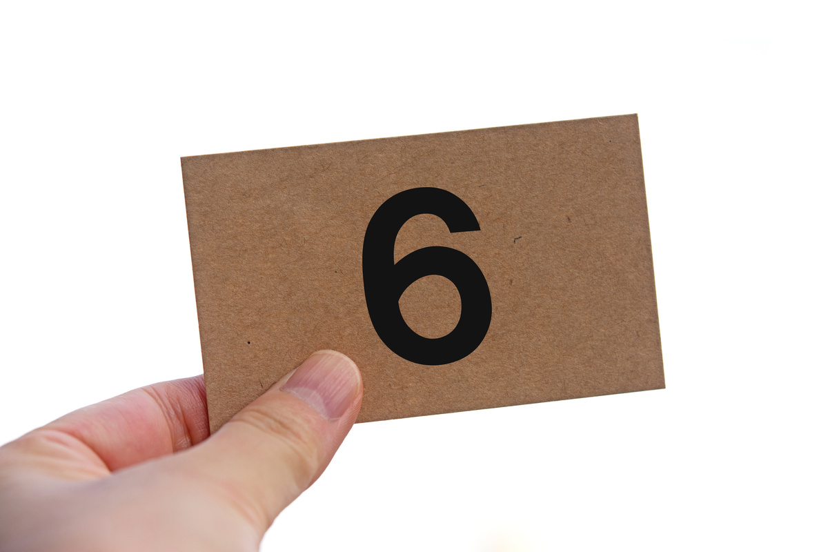Pessoa segurando pequeno papel com número 6 estampado em preto.