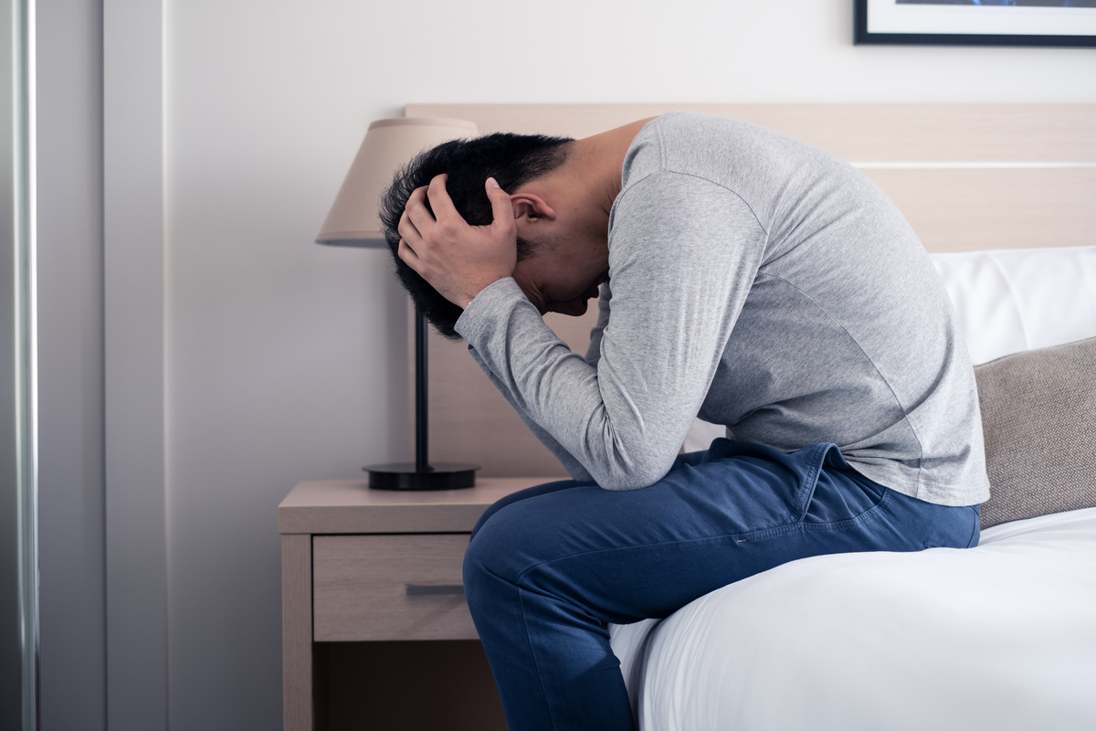 Homem sentado na cama enquanto tem as duas mãos na cabeça e o rosto baixo, aparentando chateação e representando a instabilidade emocional de um homem de Câncer.