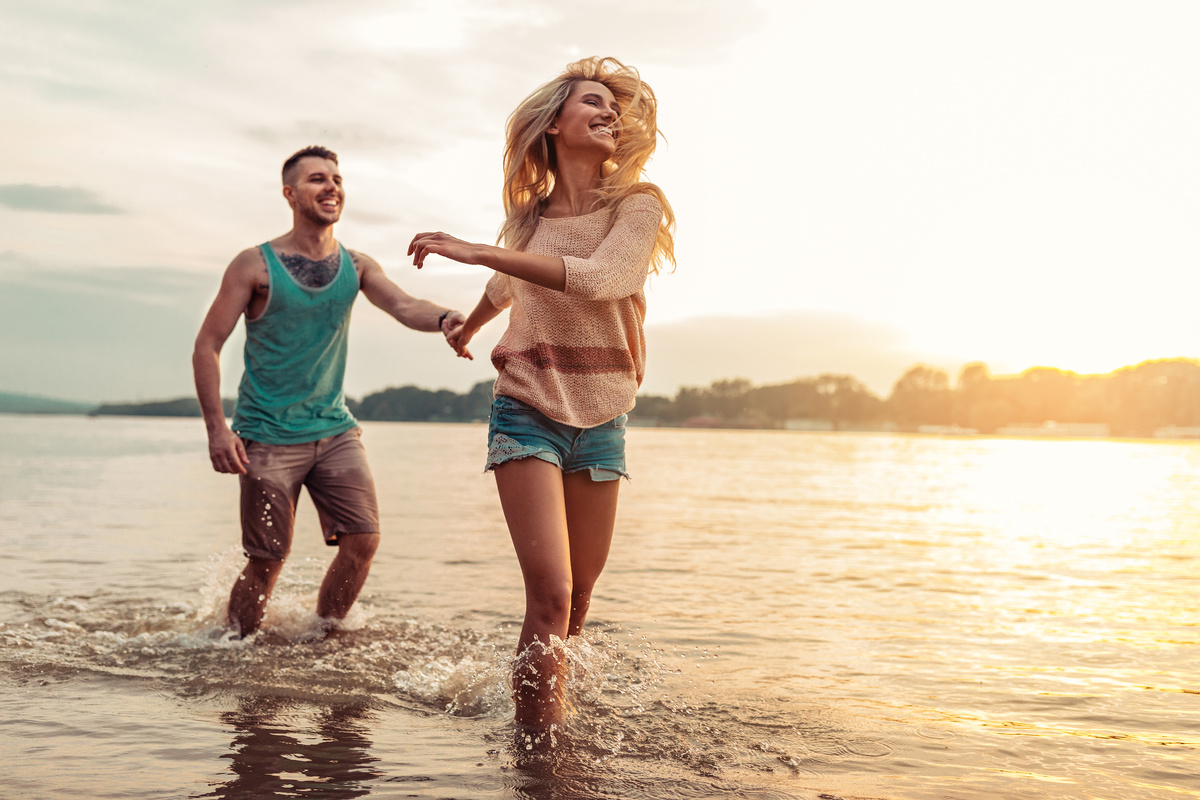 Casal de homem e mulher correndo pela praia enquanto sorriem, representando a combinação Leão e Sagitário.