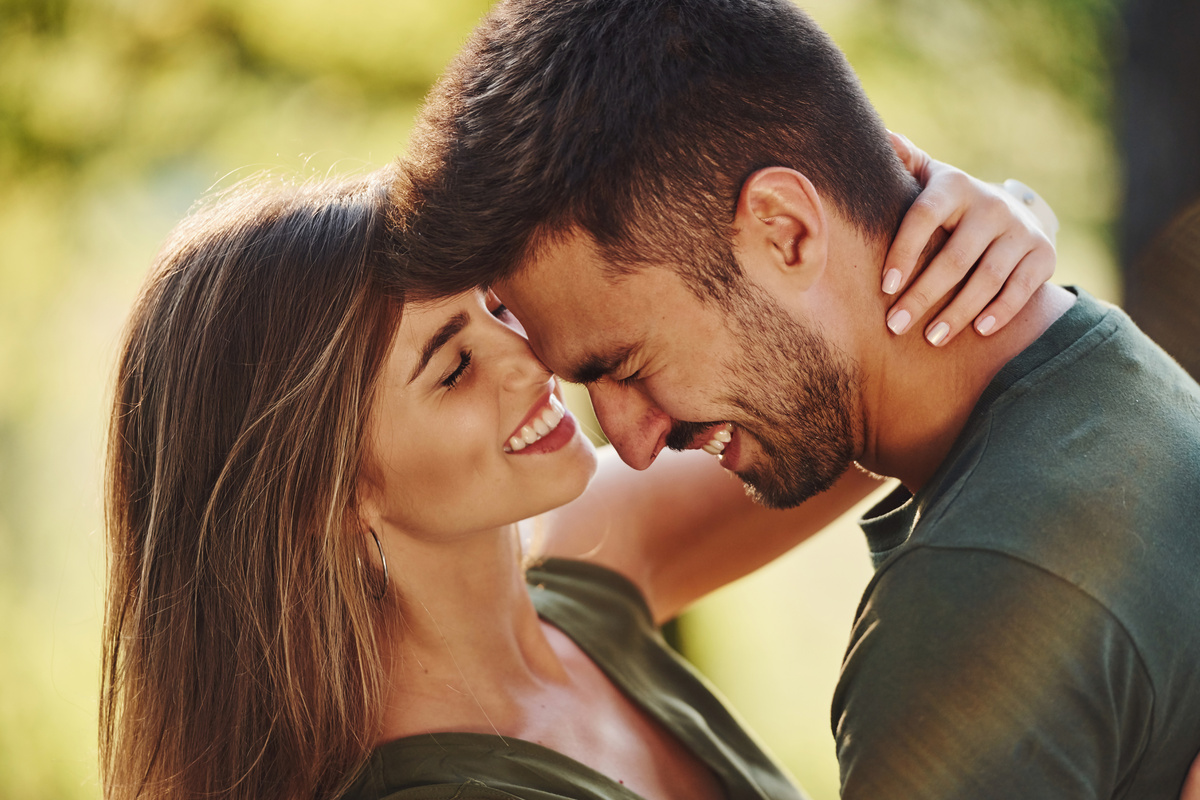 Homem e mulher se abraçando enquanto sorriem largamente um para o outro, ambos de olhos fechados, representando um relacionamento harmonioso com o leonino.