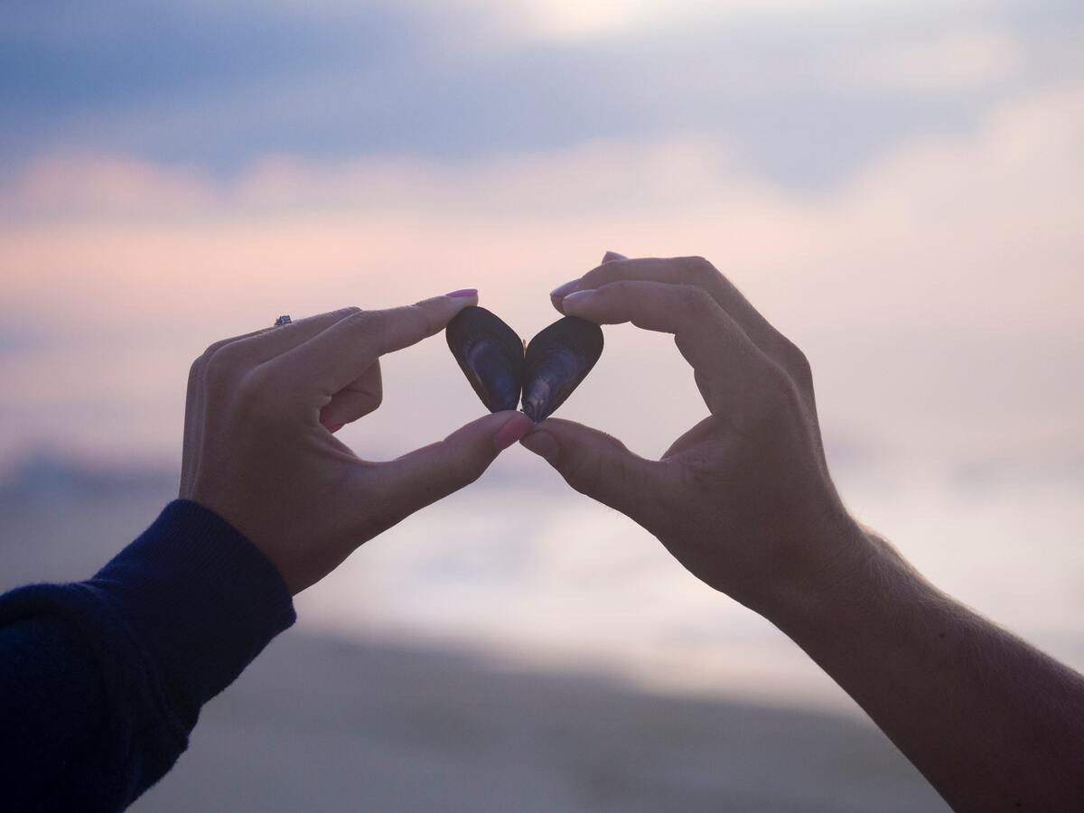 Casal segurando duas conchas que juntas formam a imagem de um coração.