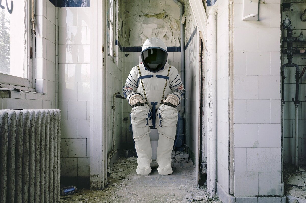 Astronauta sentado em banheiro sujo