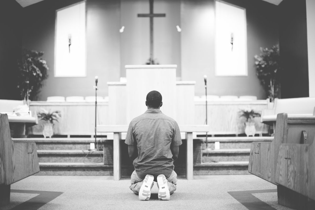 Homem orando de joelhos em igreja