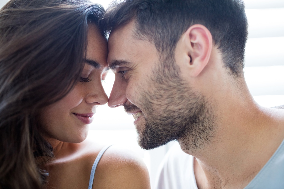 Homem e mulher com as testas juntas, ambos sorrindo carinhosamente, representando a intimidade entre Sagitário e Aquário.