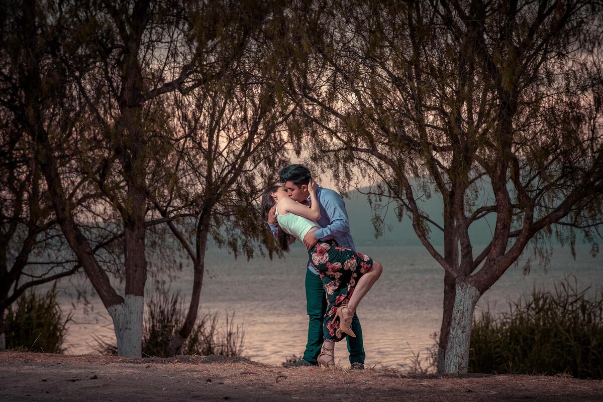 Casal de mulher e homem se beijando em meio às árvores.