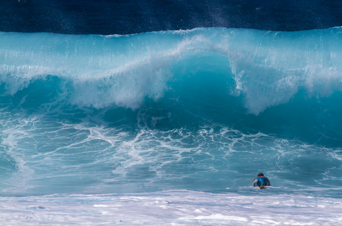 Pessoa nadando dentro de ondas grandes e azuladas.